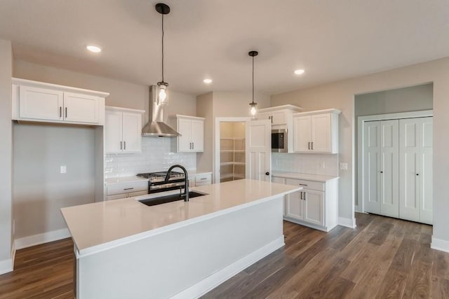 kitchen featuring wall chimney exhaust hood, white cabinetry, and an island with sink