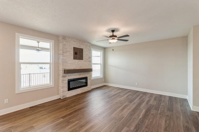 unfurnished living room with a textured ceiling, ceiling fan, a fireplace, and dark wood-type flooring