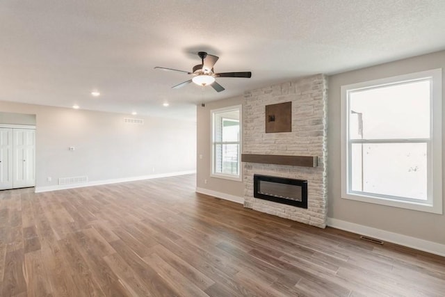 unfurnished living room featuring wood-type flooring, a textured ceiling, a stone fireplace, and ceiling fan