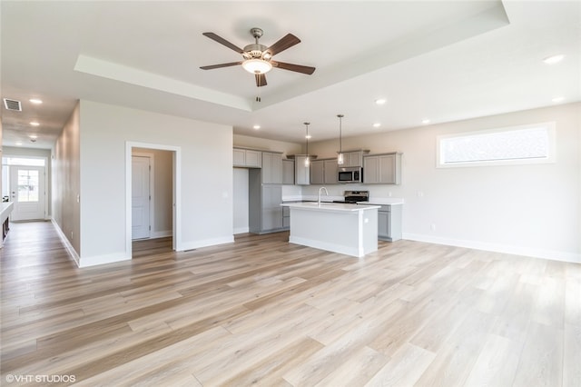 kitchen featuring a kitchen island with sink, hanging light fixtures, gray cabinets, appliances with stainless steel finishes, and light hardwood / wood-style floors