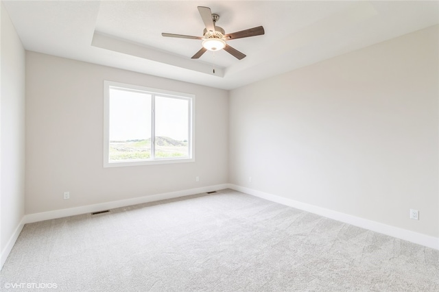 empty room with carpet, a tray ceiling, and ceiling fan