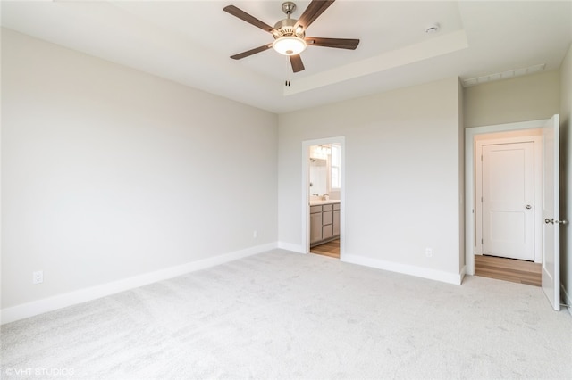 unfurnished bedroom featuring a tray ceiling, light colored carpet, connected bathroom, and ceiling fan