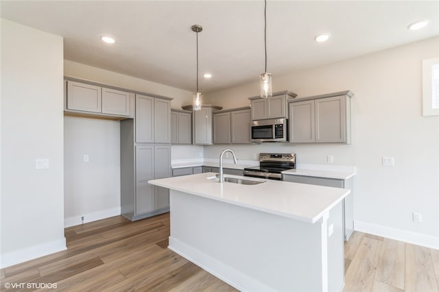 kitchen with a center island with sink, appliances with stainless steel finishes, light wood-type flooring, sink, and decorative light fixtures