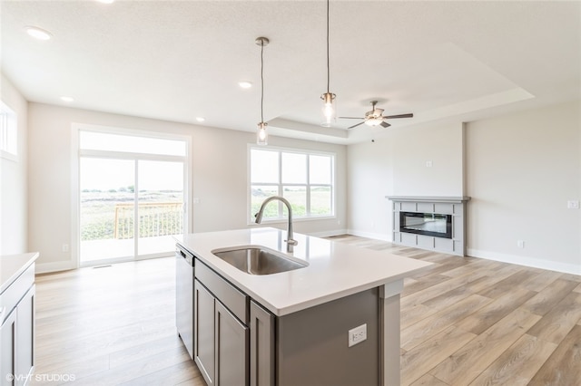 kitchen with sink, dishwasher, light hardwood / wood-style floors, decorative light fixtures, and a center island with sink