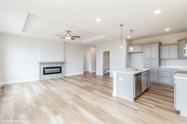 kitchen with light hardwood / wood-style floors, dishwasher, an island with sink, and a tile fireplace