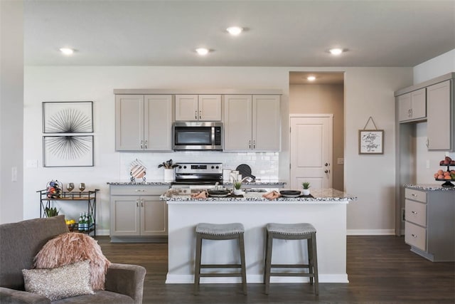 kitchen with light stone counters, stainless steel appliances, gray cabinets, dark hardwood / wood-style floors, and an island with sink