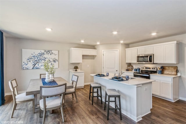 kitchen with a kitchen breakfast bar, a center island, appliances with stainless steel finishes, white cabinetry, and dark hardwood / wood-style flooring