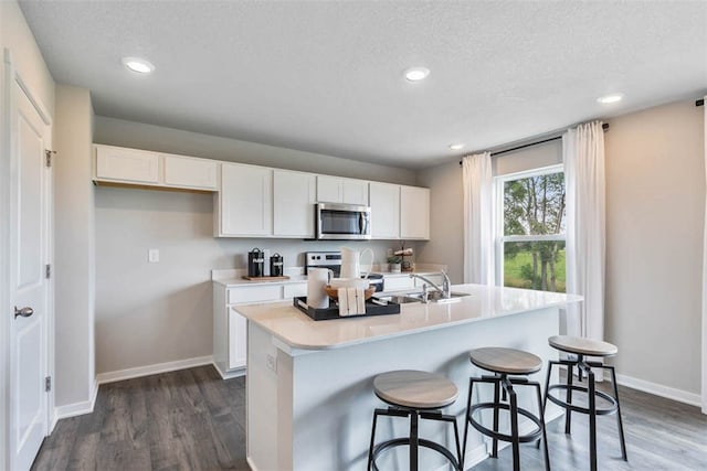 kitchen with a center island with sink, a breakfast bar area, white cabinetry, dark hardwood / wood-style floors, and sink