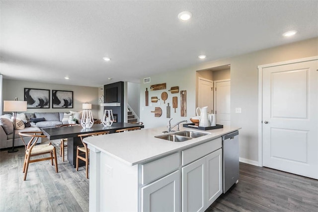 kitchen featuring dark hardwood / wood-style floors, sink, stainless steel dishwasher, a center island with sink, and a textured ceiling