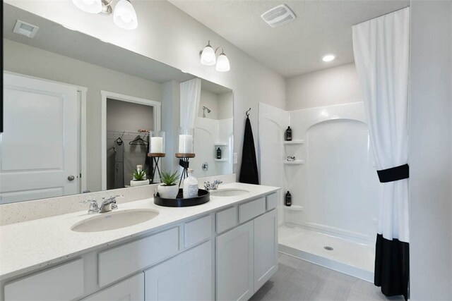 bathroom with vanity with extensive cabinet space, dual sinks, tile floors, and a shower
