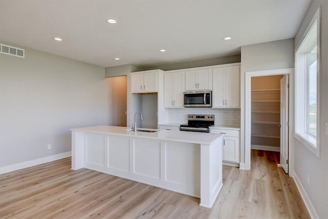 kitchen with sink, an island with sink, appliances with stainless steel finishes, tasteful backsplash, and white cabinetry