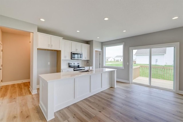 kitchen with sink, stainless steel appliances, a kitchen island with sink, white cabinets, and light wood-type flooring