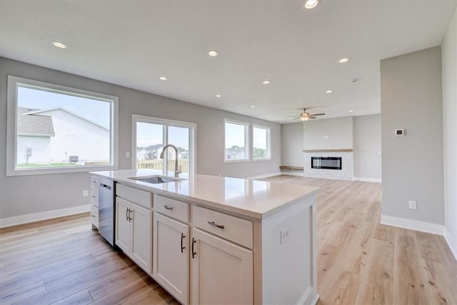 kitchen with sink, stainless steel dishwasher, a center island with sink, and light wood-type flooring