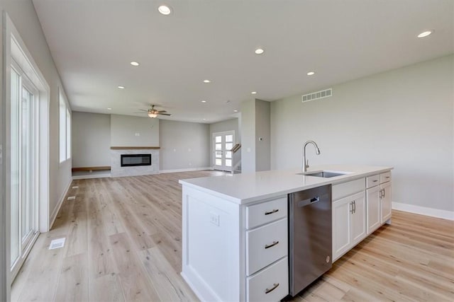 kitchen featuring light wood-type flooring, sink, dishwasher, white cabinets, and an island with sink