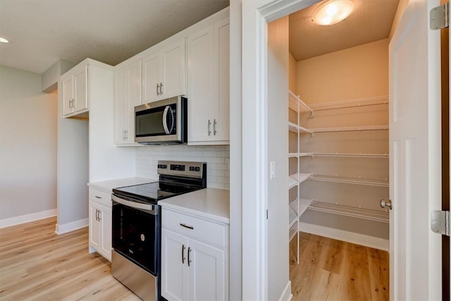 kitchen featuring light hardwood / wood-style flooring, white cabinetry, stainless steel appliances, and tasteful backsplash