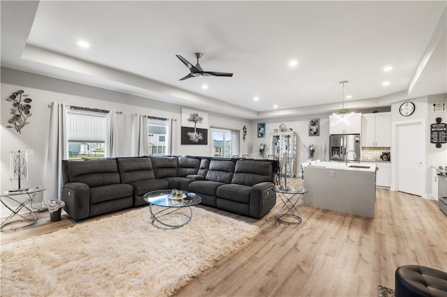 living room featuring a raised ceiling, light hardwood / wood-style floors, ceiling fan, and sink