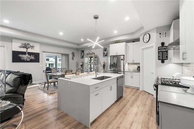 kitchen with backsplash, a kitchen island with sink, light wood-type flooring, white cabinets, and pendant lighting