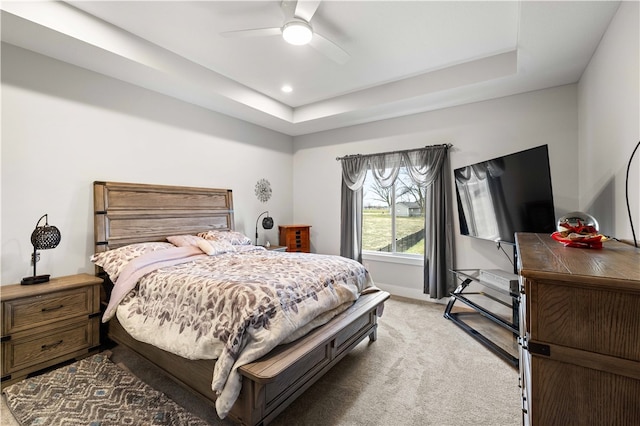 bedroom featuring light colored carpet, a raised ceiling, and ceiling fan