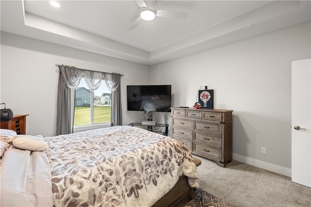 bedroom featuring a raised ceiling, light colored carpet, and ceiling fan