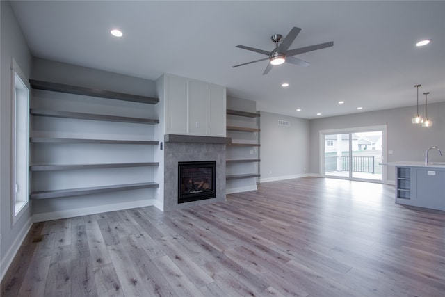 unfurnished living room featuring ceiling fan with notable chandelier, a tiled fireplace, and light hardwood / wood-style floors