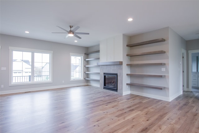 unfurnished living room with a tiled fireplace, light hardwood / wood-style floors, and ceiling fan