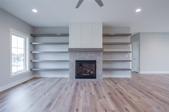 unfurnished living room featuring a tiled fireplace, light wood-type flooring, and ceiling fan