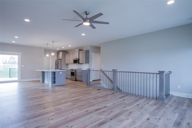 kitchen with hanging light fixtures, gray cabinets, a breakfast bar area, an island with sink, and light hardwood / wood-style floors