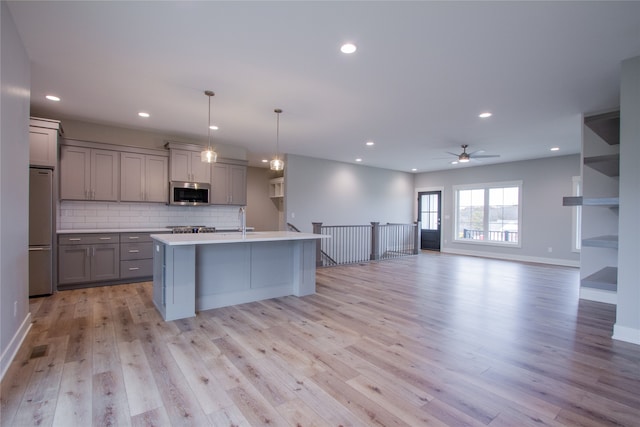 kitchen with a center island with sink, appliances with stainless steel finishes, light wood-type flooring, and gray cabinets