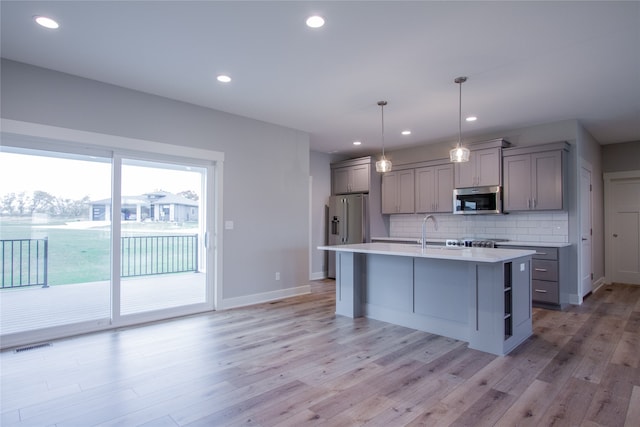 kitchen with gray cabinets, appliances with stainless steel finishes, hanging light fixtures, and light hardwood / wood-style flooring