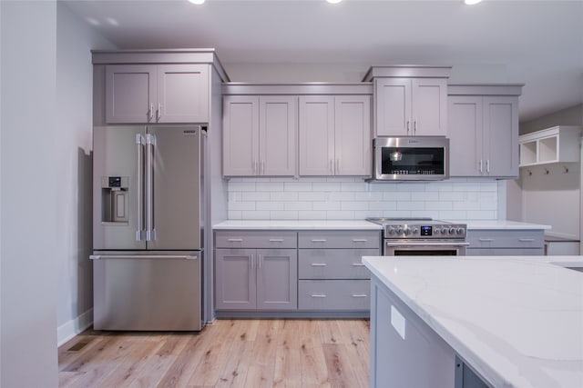 kitchen featuring decorative backsplash, light stone counters, stainless steel appliances, and light hardwood / wood-style floors