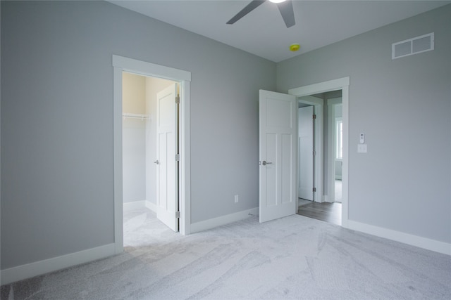 unfurnished bedroom featuring a spacious closet, light colored carpet, a closet, and ceiling fan