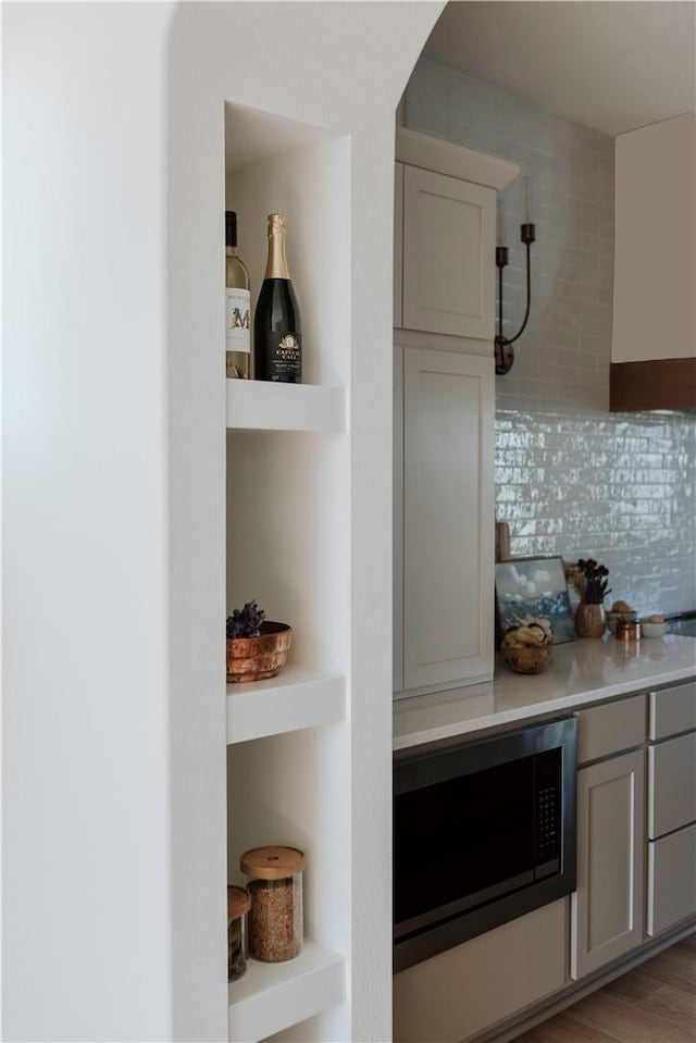 interior space featuring gray cabinetry, tasteful backsplash, black microwave, and light wood-type flooring