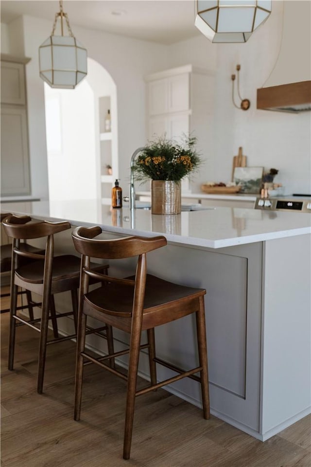kitchen with wall chimney exhaust hood, a breakfast bar, sink, pendant lighting, and hardwood / wood-style floors