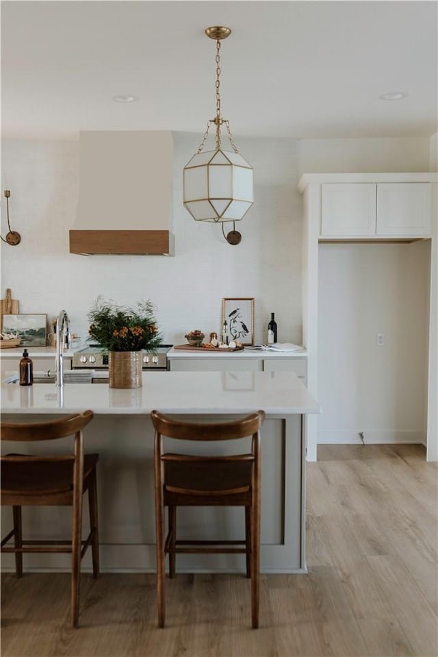 kitchen featuring pendant lighting, custom exhaust hood, a breakfast bar, and white cabinets
