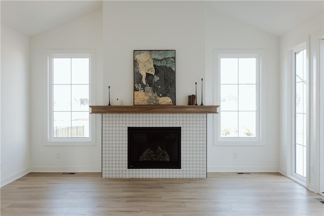 unfurnished living room with a tile fireplace, lofted ceiling, and light wood-type flooring