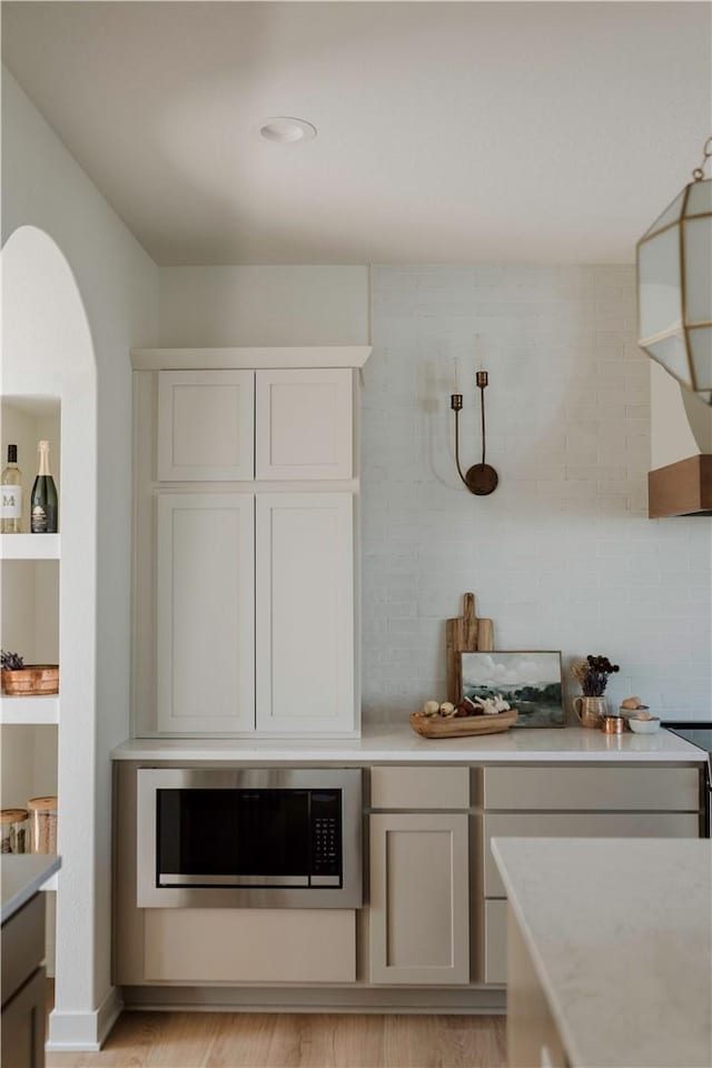 kitchen featuring built in microwave, backsplash, white cabinetry, and light hardwood / wood-style flooring