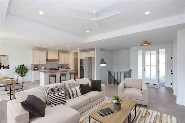 living room with light wood-type flooring, a tray ceiling, and ceiling fan