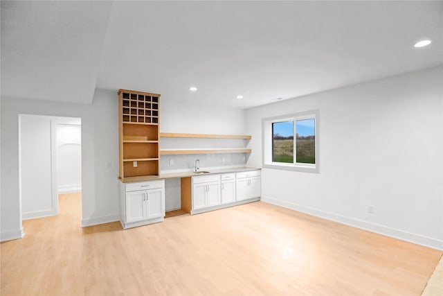 interior space featuring white cabinetry, light hardwood / wood-style flooring, built in desk, and sink