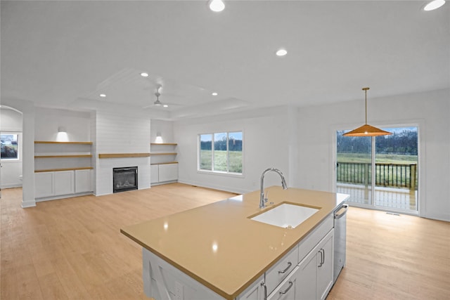 kitchen featuring stainless steel dishwasher, sink, white cabinets, hanging light fixtures, and an island with sink