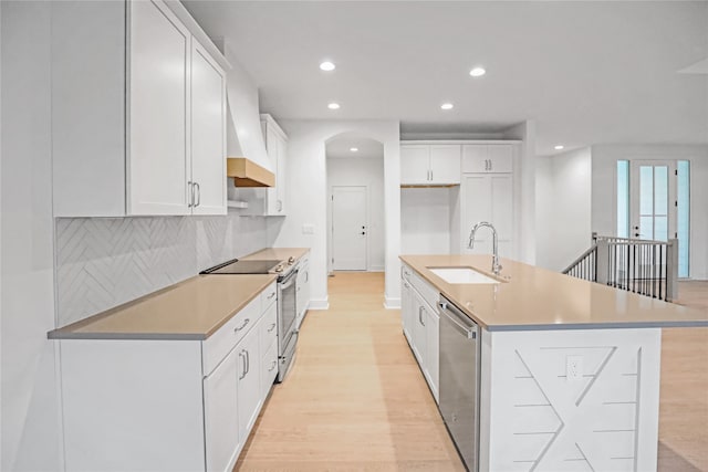 kitchen featuring appliances with stainless steel finishes, custom exhaust hood, sink, a center island with sink, and white cabinetry