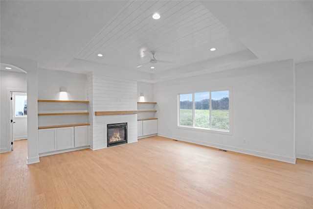 unfurnished living room featuring ceiling fan, a large fireplace, a raised ceiling, wood ceiling, and light wood-type flooring