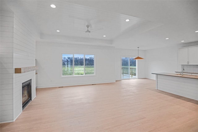 1772 Highland Cir SW, Altoona, IA 50009 - unfurnished living room featuring a raised ceiling, a sink, a ceiling fan, light wood-style flooring, and a large fireplace