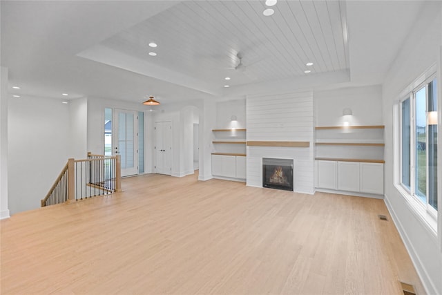 unfurnished living room with ceiling fan, a large fireplace, wooden ceiling, light hardwood / wood-style flooring, and a tray ceiling