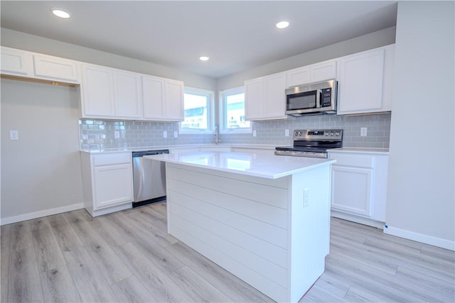 kitchen with stainless steel appliances, white cabinetry, a kitchen island, and light hardwood / wood-style flooring