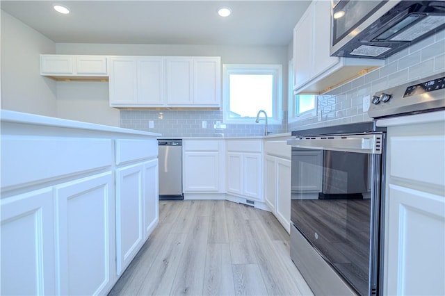 kitchen with tasteful backsplash, white cabinets, light hardwood / wood-style floors, and appliances with stainless steel finishes