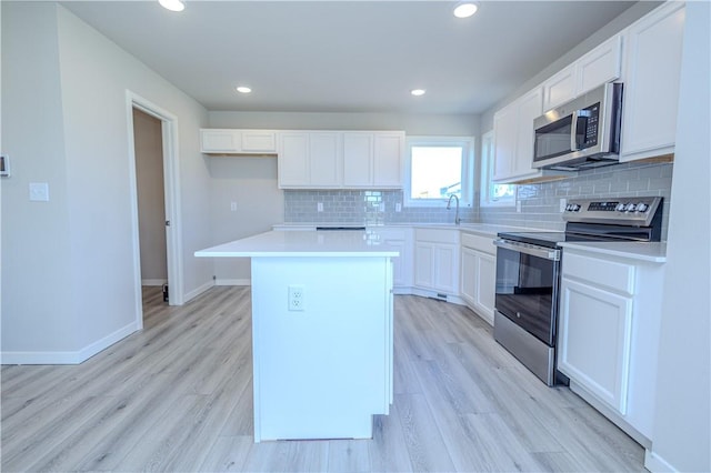 kitchen with stainless steel appliances, a kitchen island, tasteful backsplash, white cabinets, and light wood-type flooring