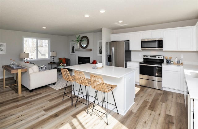 kitchen featuring white cabinets, appliances with stainless steel finishes, light hardwood / wood-style flooring, and a breakfast bar area