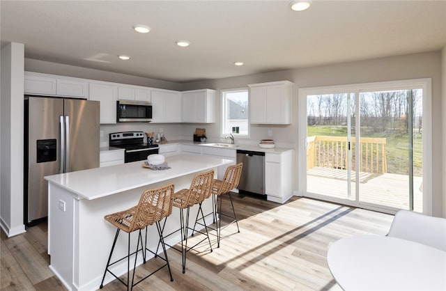 kitchen with a kitchen bar, a kitchen island, stainless steel appliances, white cabinetry, and light wood-type flooring