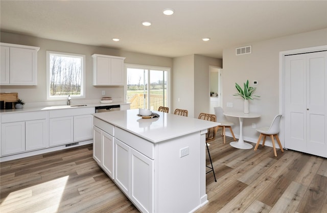 kitchen featuring a center island, a breakfast bar, white cabinetry, sink, and light hardwood / wood-style floors