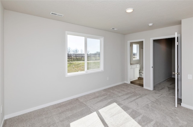 unfurnished bedroom featuring light carpet and connected bathroom